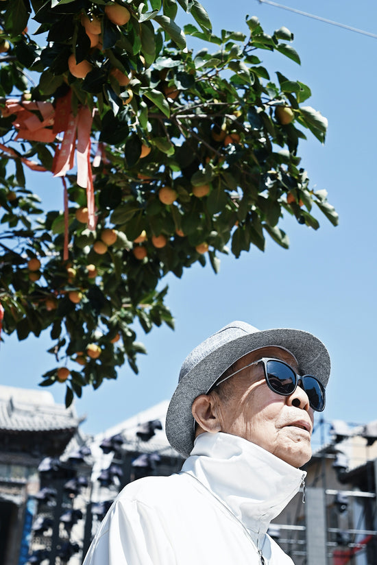 a man wearing sunglasses and a hat standing under a tree with orange fruits