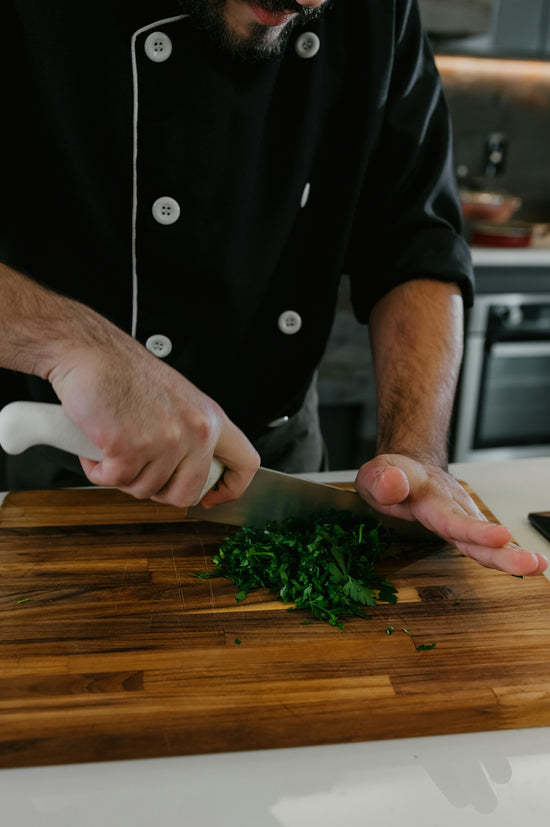A man in a chef's outfit chopping greens on a cutting board