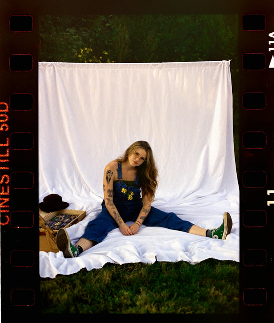 Woman in overalls sits on white cloth outdoors.