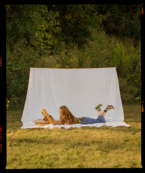 Young woman reading on a blanket outdoors.