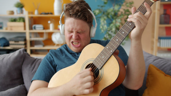 Man enthusiastically playing acoustic guitar with headphones on.