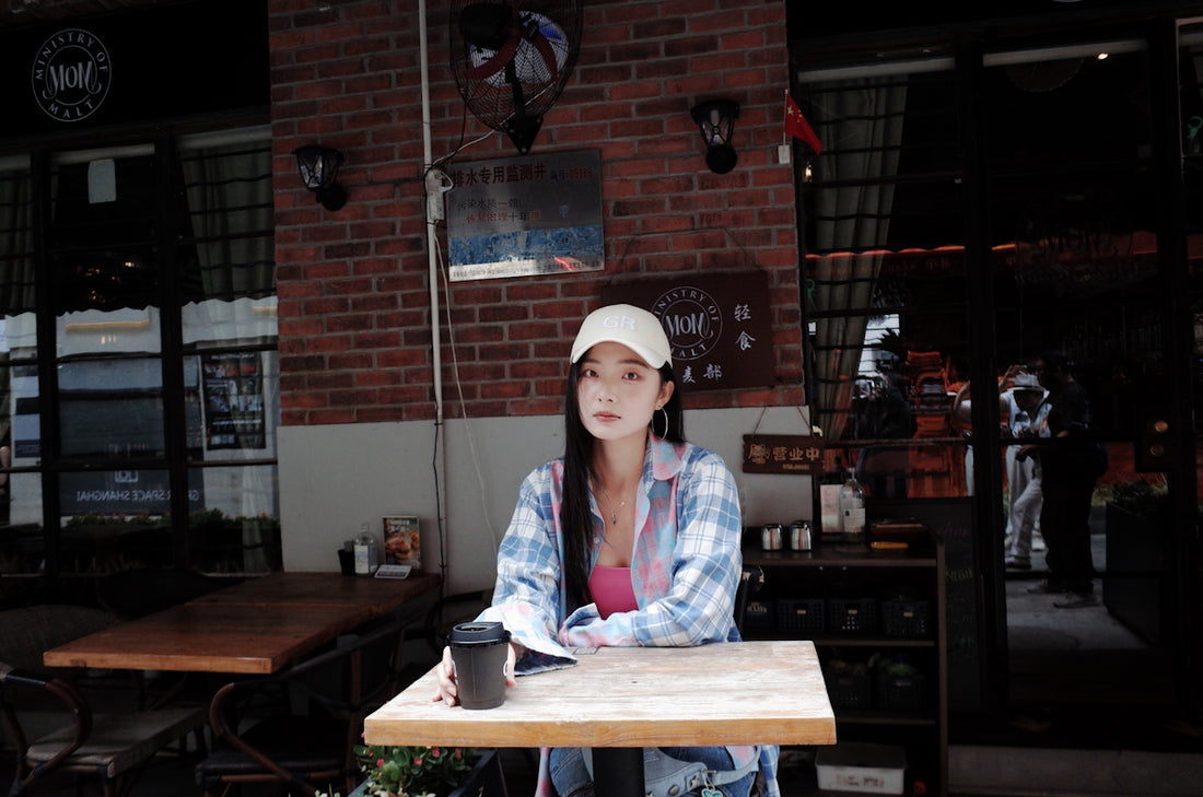 Woman in cap sits at cafe table with coffee.