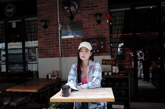 Woman in cap sits at cafe table with coffee.