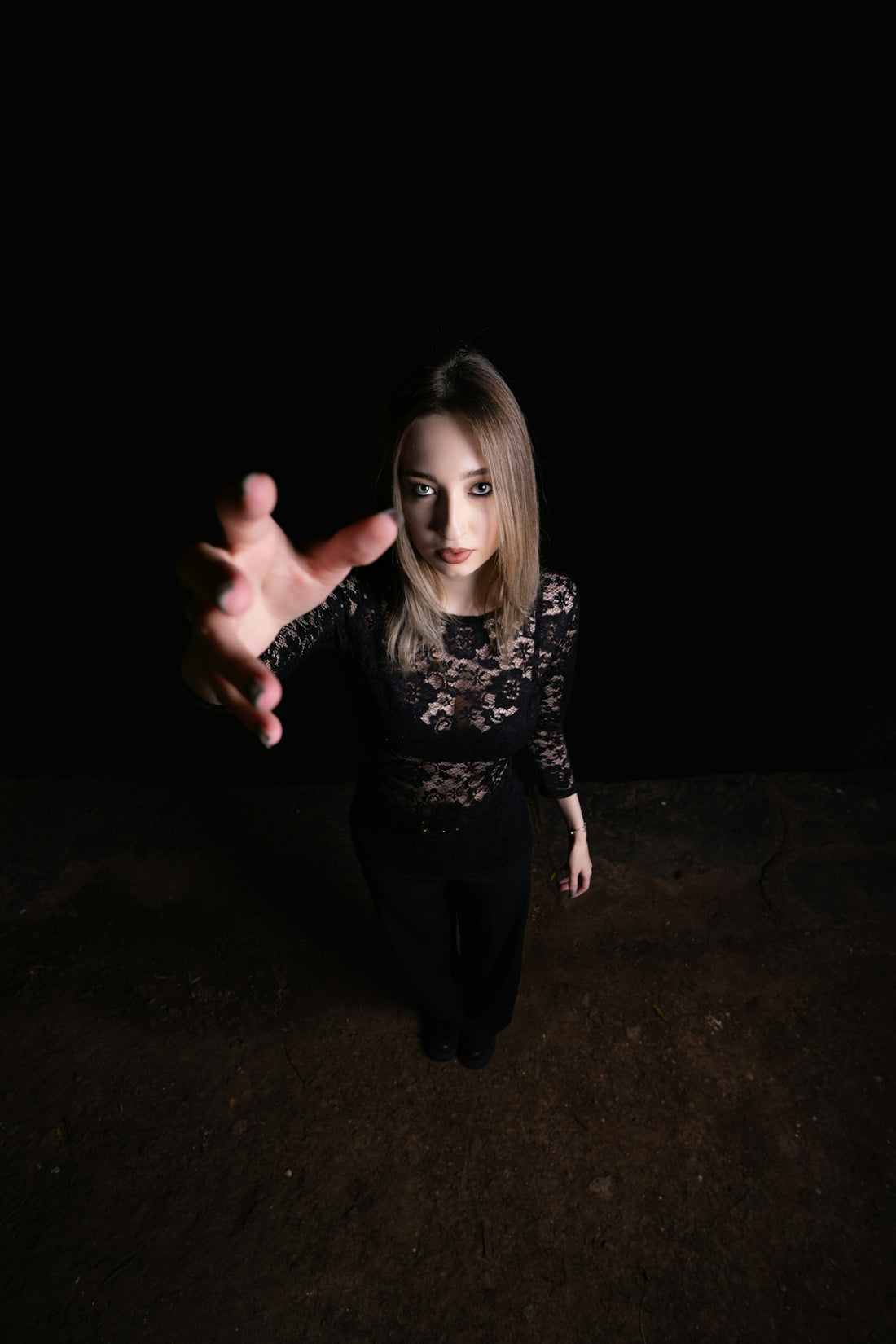 Woman in black lace reaching out in darkness