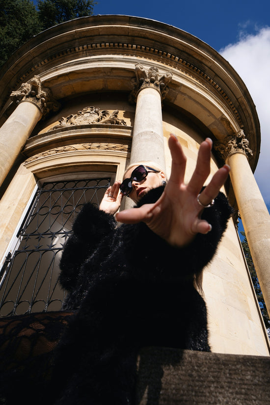 Woman in sunglasses reaches out near building.