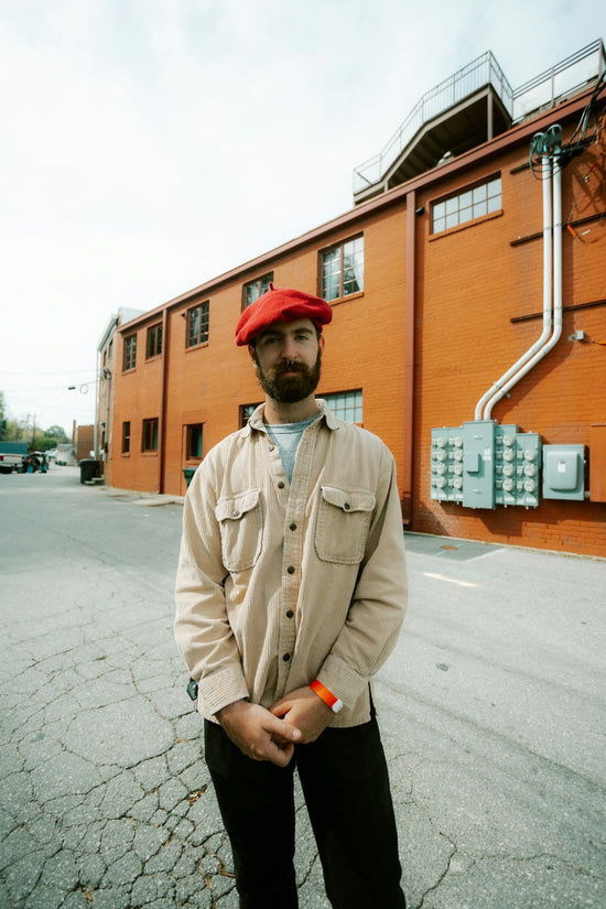 Man in red beret stands outside brick building.