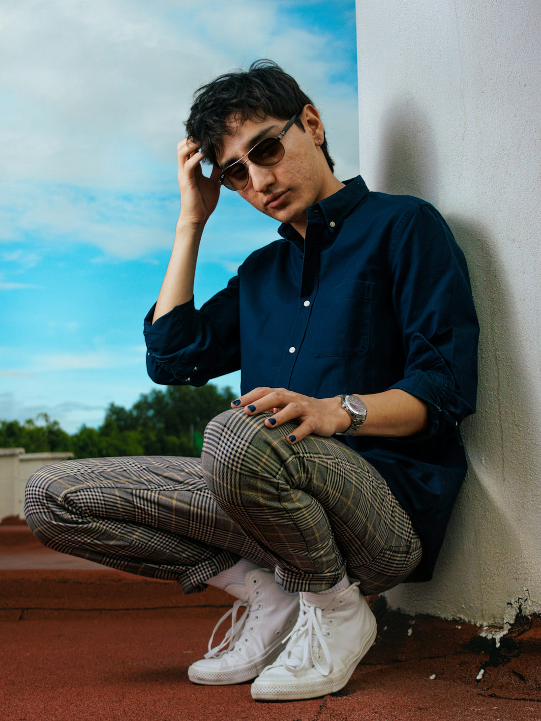 Man in sunglasses crouches against a wall