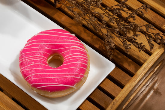 Pink frosted donut with white stripes on plate