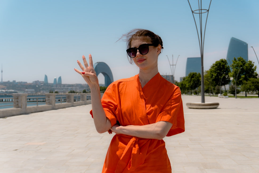 Woman in orange dress waves with four fingers.