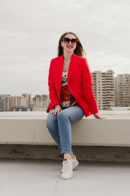 Woman in red blazer and jeans sitting outdoors