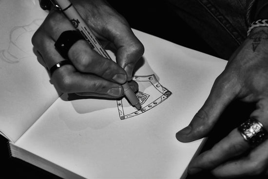 Hands drawing an axe design in a sketchbook
