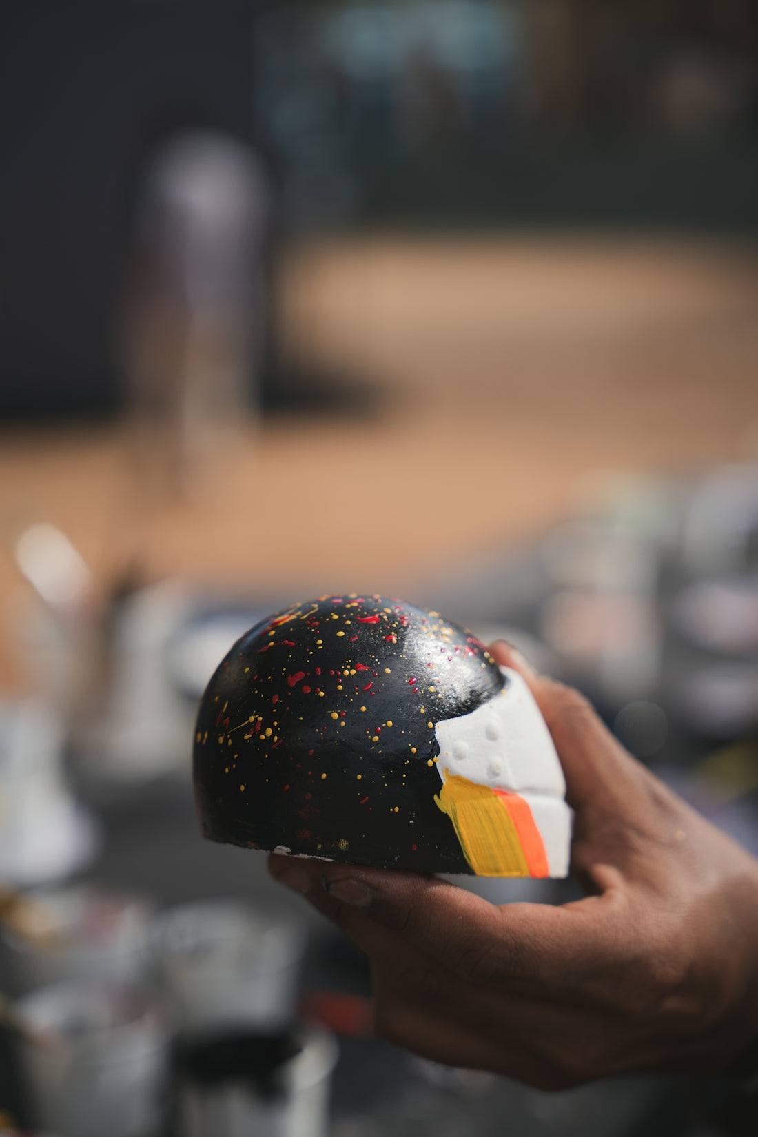 Hand holding a painted chocolate sphere with colorful speckles.