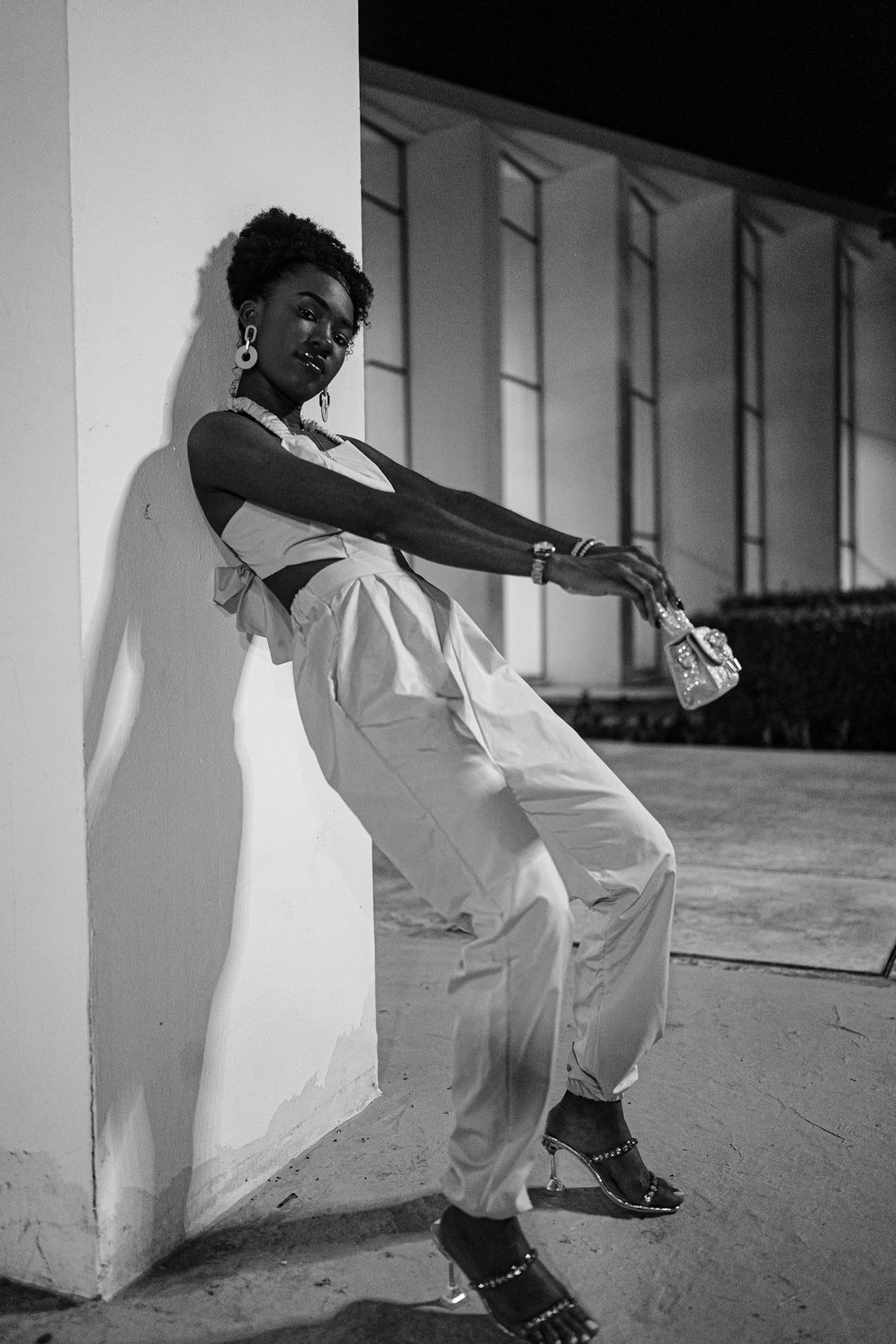 A woman poses leaning against a wall at night.