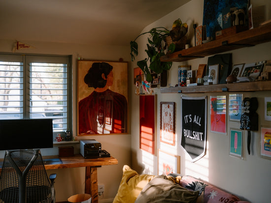 Sunlit room with art, plants, and a desk.