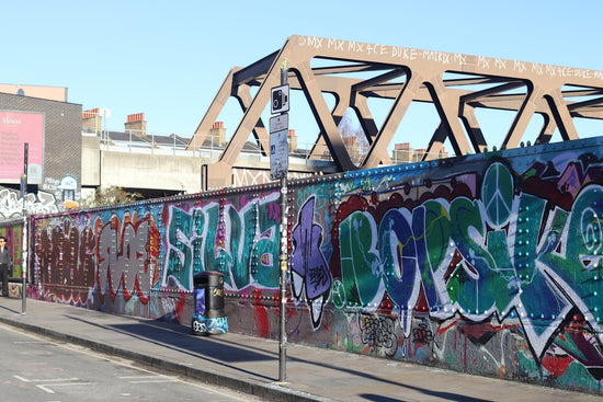 Graffiti art covers a long wall under a bridge.
