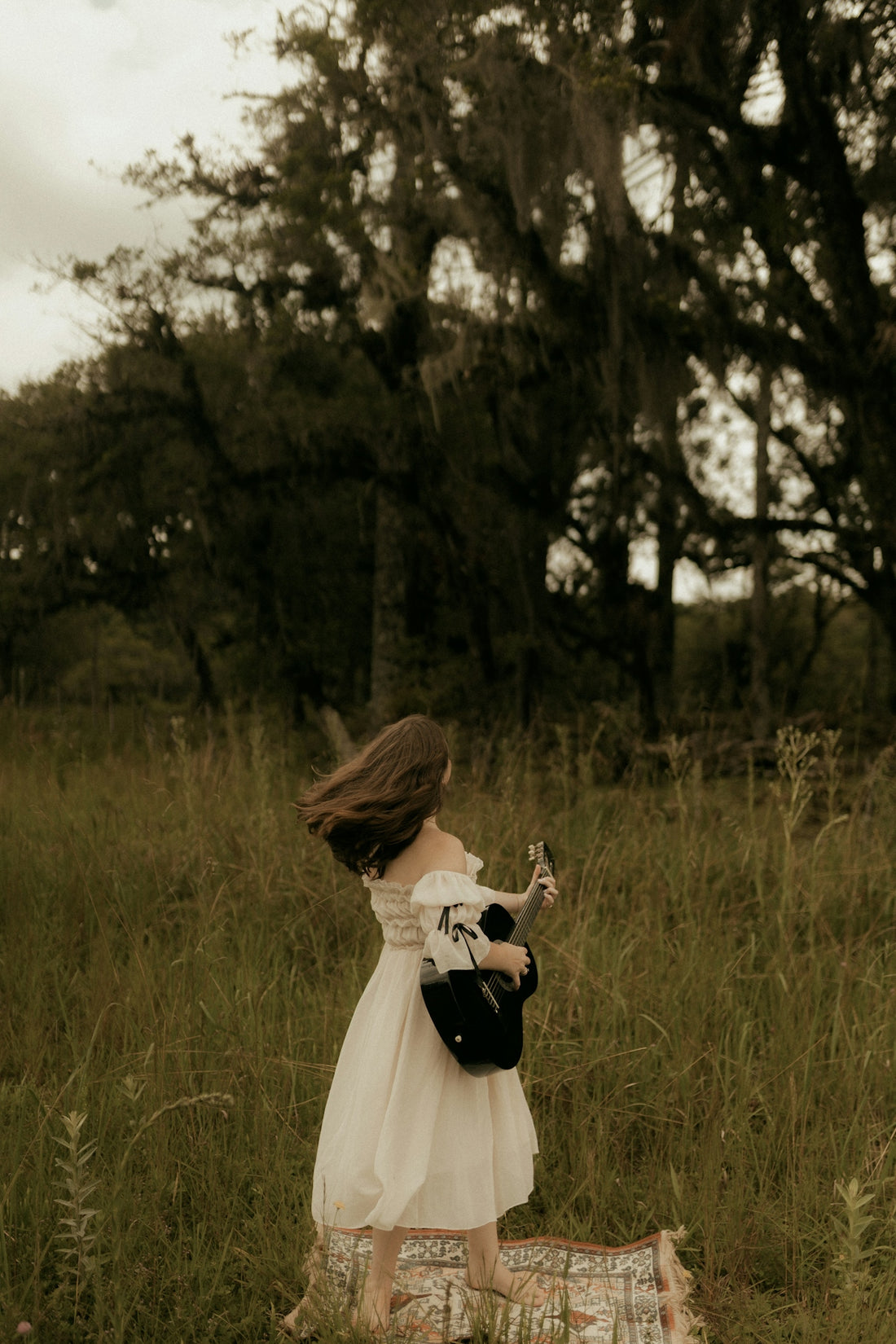 Woman in white dress playing guitar in grassy field