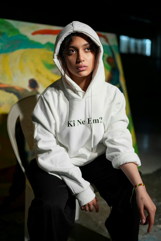Young woman in a white hoodie sits indoors.