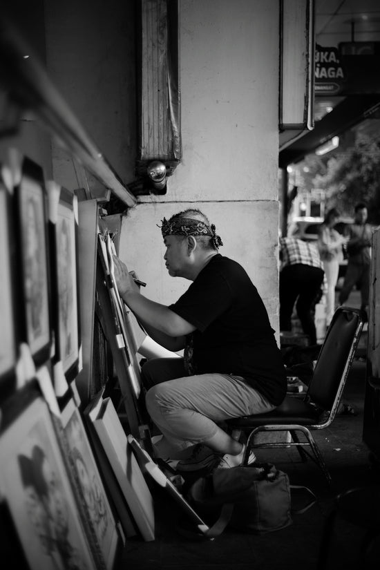 Artist drawing on easel outdoors with framed art displayed