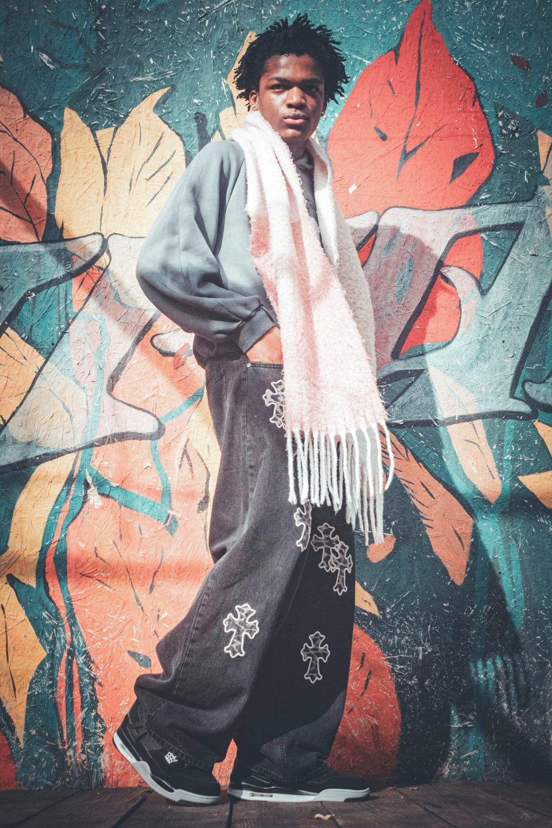 Young man posing against graffiti wall wearing baggy jeans.