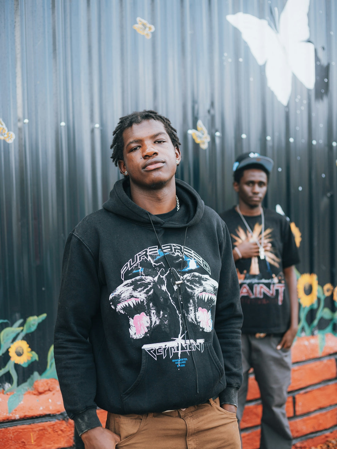 Two young men stand in front of a mural
