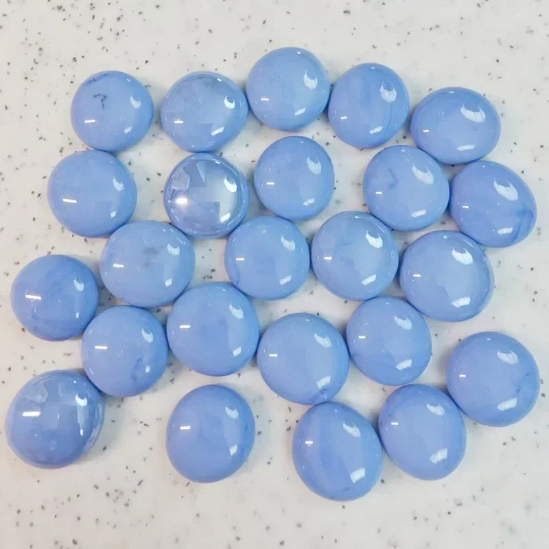 Glossy light blue round glass marbles on speckled white surface