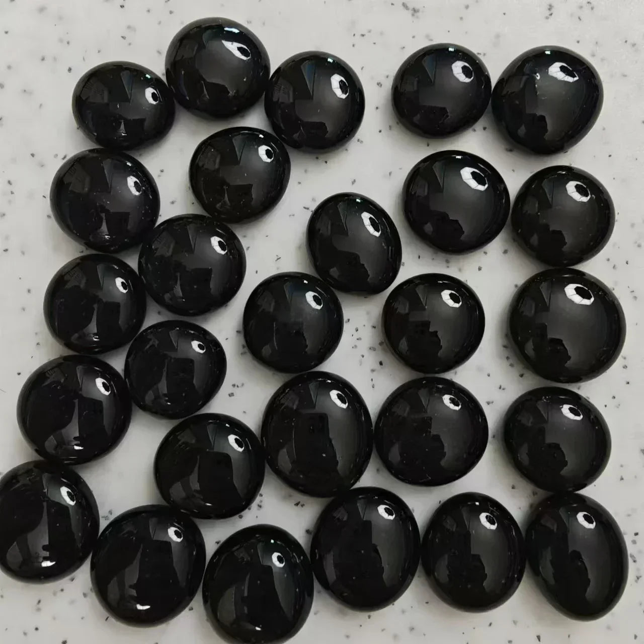 Array of polished black obsidian stones on a speckled white surface