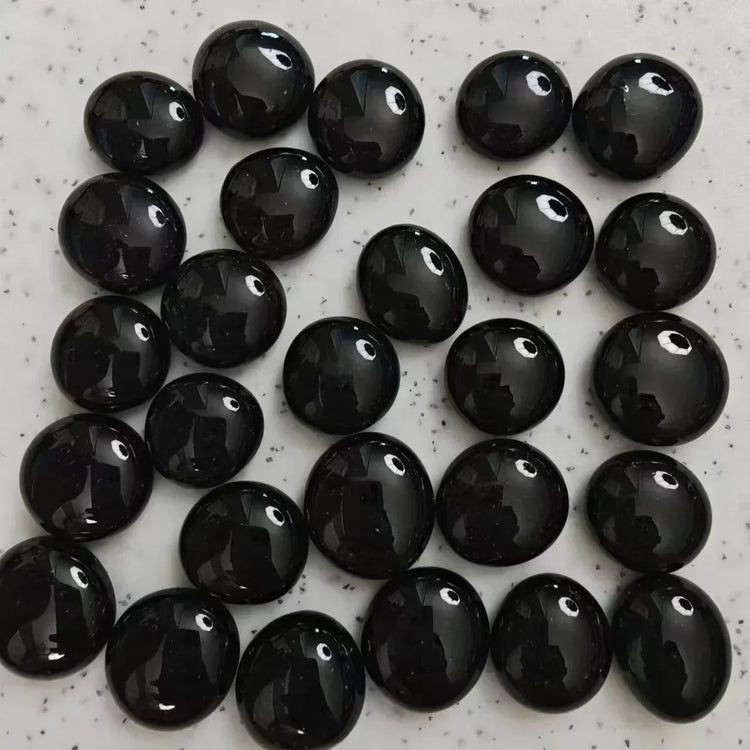 Array of polished black obsidian stones on a speckled white surface